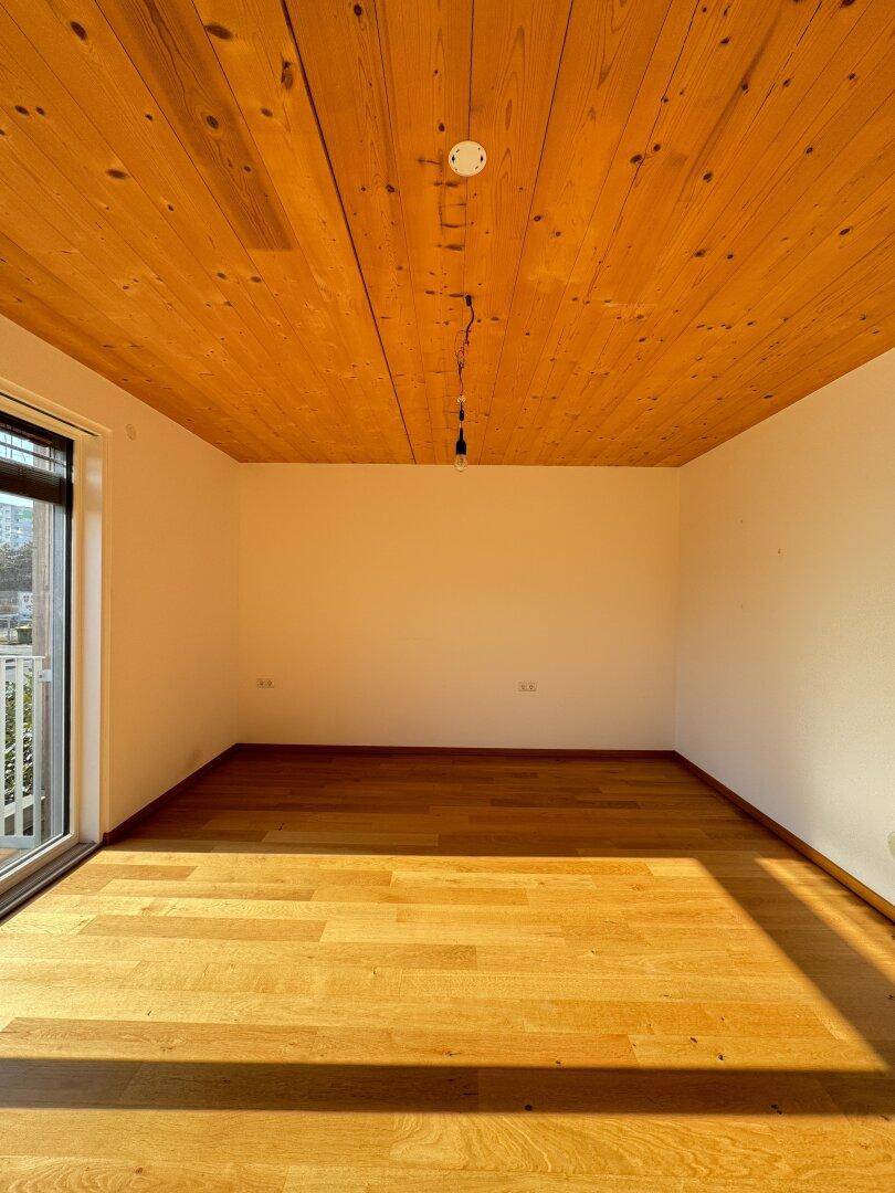 Großzügiger Raum mit Holzbalkendecke und Parkettboden, bietet viel natürliches Licht.