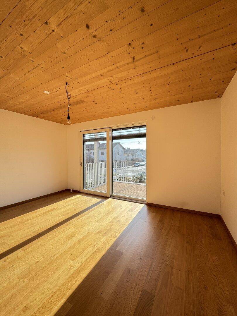 Heller Wohnraum mit Holzbalkendecke, Parkettboden und direktem Zugang zum Balkon.