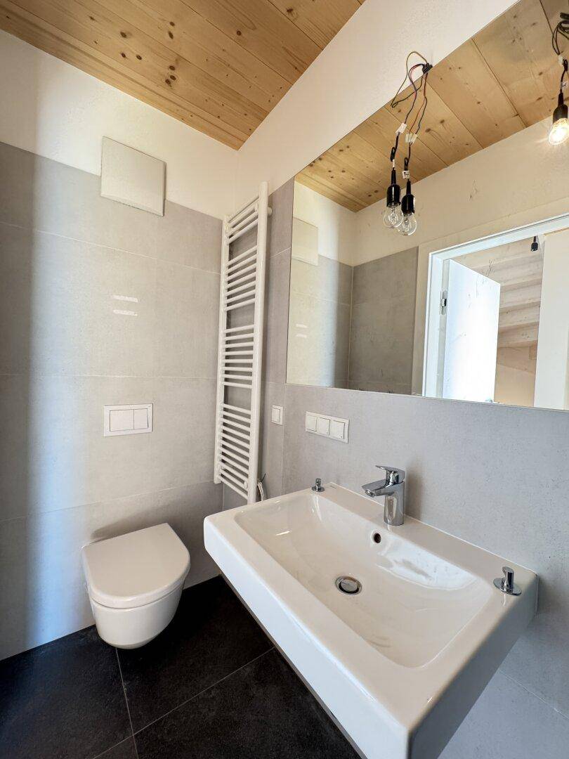 Helles Badezimmer mit wandhängendem WC, Einzelwaschbecken, beheiztem Handtuchhalter und großem Spiegel.