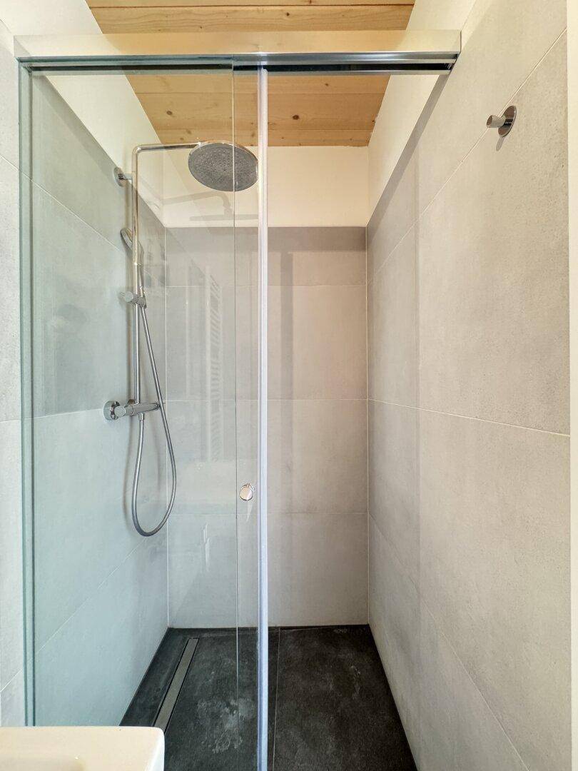 Moderne begehbare Dusche mit Glasabtrennung, Regenduschkopf und dunklem Fliesenboden.