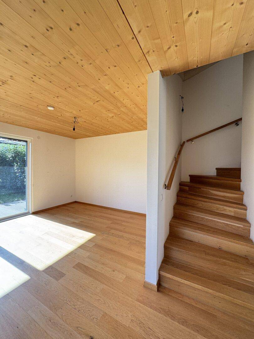 Offener Wohnbereich mit Holzbalkendecke, Parkettboden und Treppenzugang zum Garten.