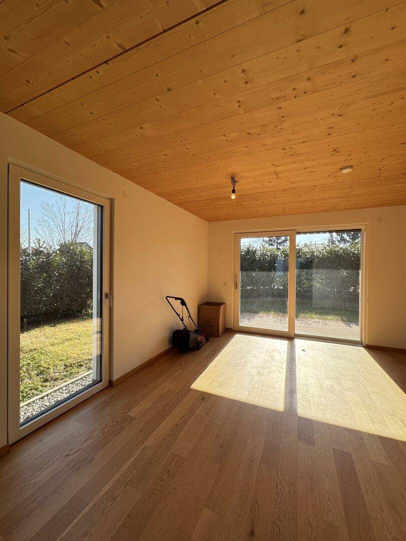 Lichtdurchfluteter Wohnraum mit Holzbalkendecke, Parkettboden und direktem Gartenzugang.
