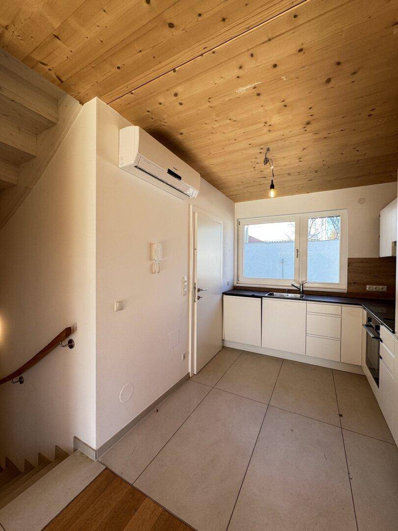 Moderne Küche mit weißen Schränken, dunkler Arbeitsplatte und Fliesenboden, neben der Treppe.
