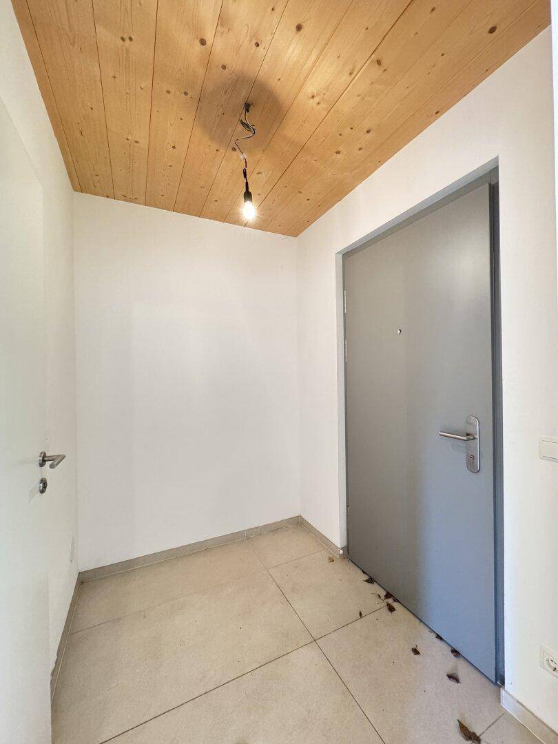 Eingangsbereich mit grauer Haustür, gefliestem Boden und einer Decke aus Holzpaneelen.