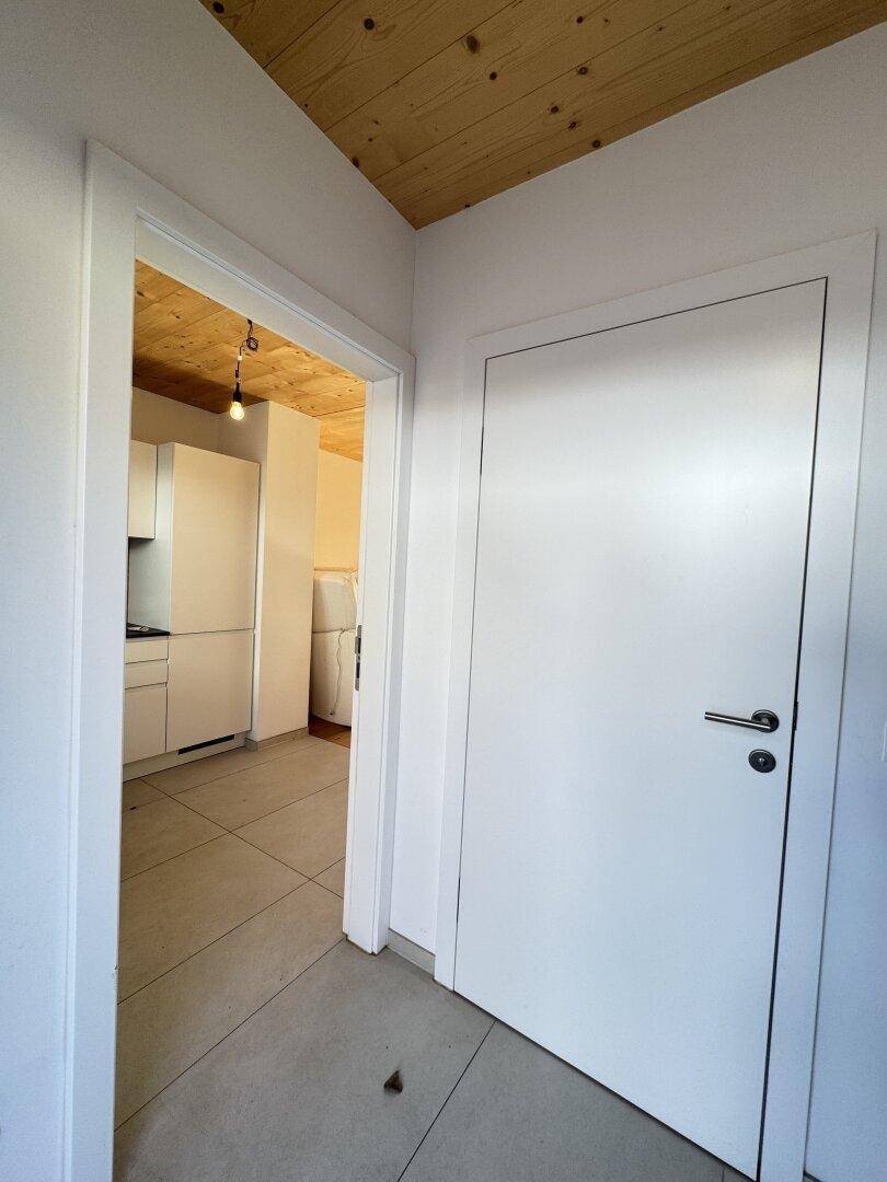 Eingangsbereich mit Blick in eine moderne Küche mit weißen Schränken und Fliesenboden.