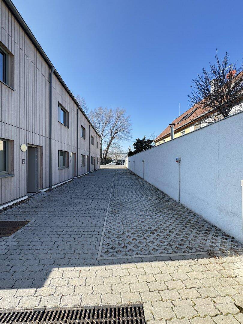Gepflasterter Weg zwischen einer Reihe von Reihenhäusern und einer hohen weißen Mauer an einem sonnigen Tag.
