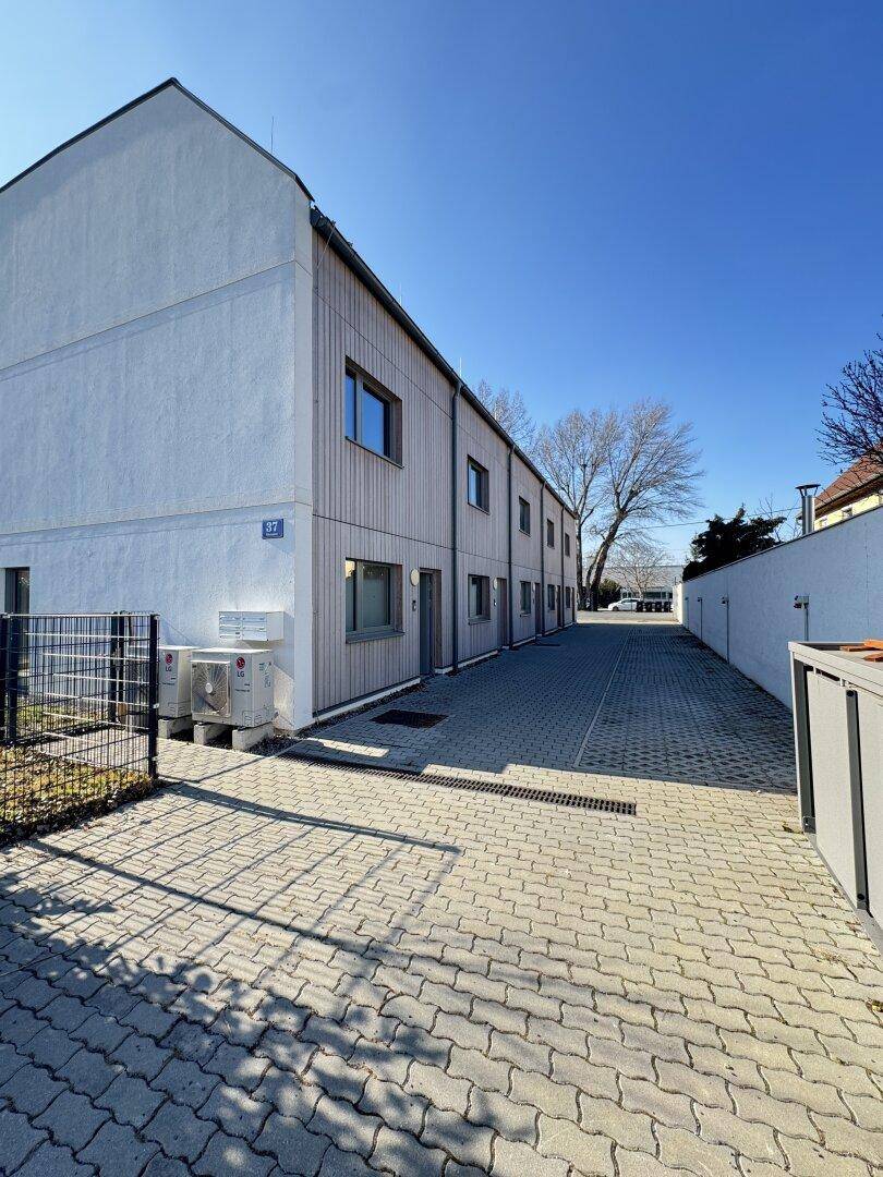 Reihe moderner Reihenhäuser mit Holzfassade und einem gepflasterten Zufahrtsweg oder Parkplatz.