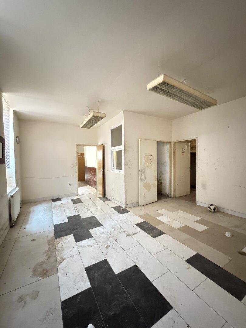 Büroraum mit auffälligem schwarz-weißem Fliesenmuster und mehreren Türen, beleuchtet von Deckenleuchten.