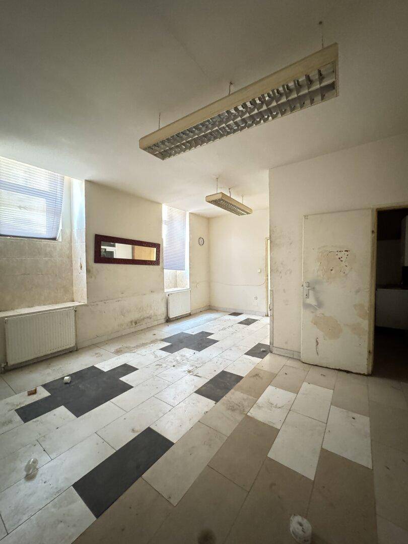 Büroraum mit schwarz-weißem Fliesenboden, Spiegel an der Wand und Fenstern mit Jalousien.