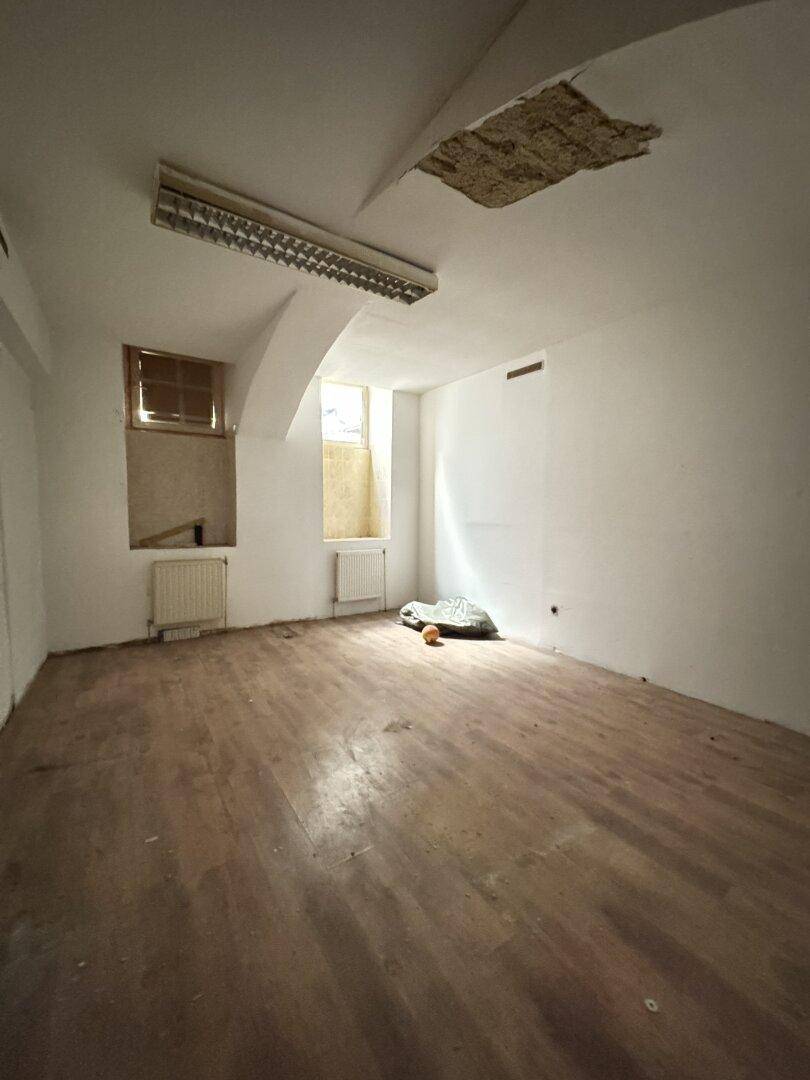 Raum mit Holzdielenboden, einem kleinen Fenster und einer beschädigten Decke, die Renovierung benötigt.