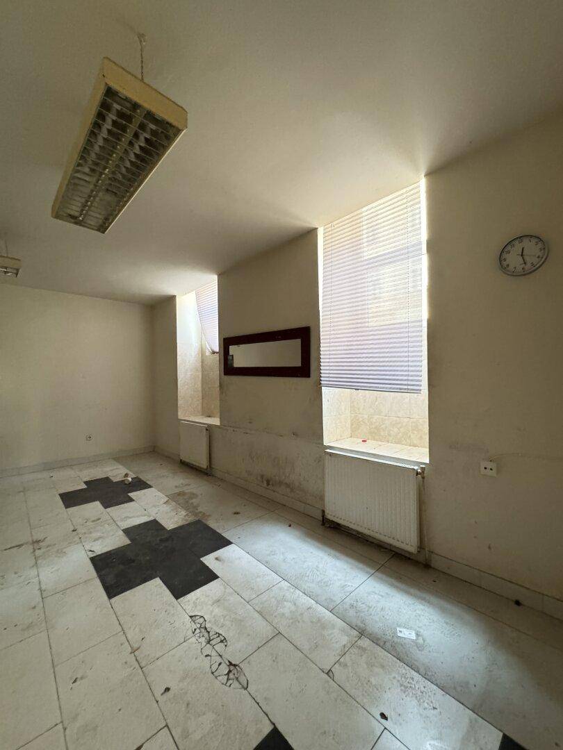 Büroraum mit schwarz-weißem Fliesenboden, einer Uhr an der Wand und Fenstern mit Jalousien.