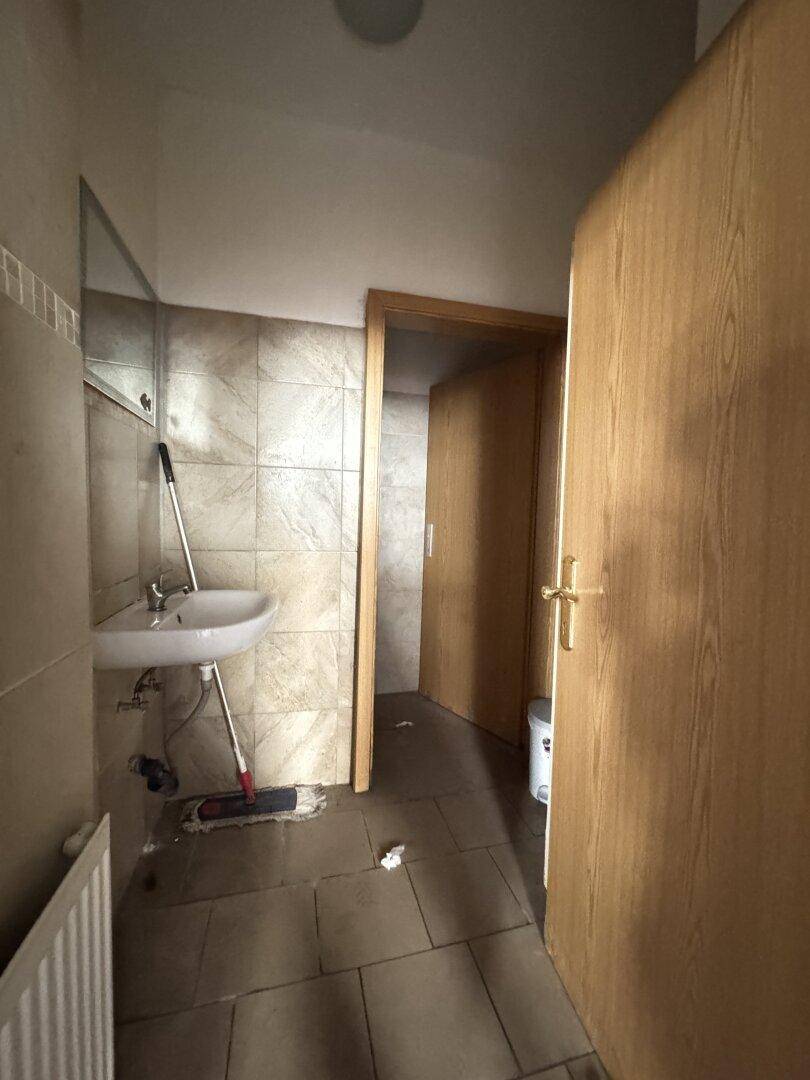 Badezimmer mit Waschbecken, Spiegel und gefliesten Wänden, in einem funktionalen, aber einfachen Zustand.