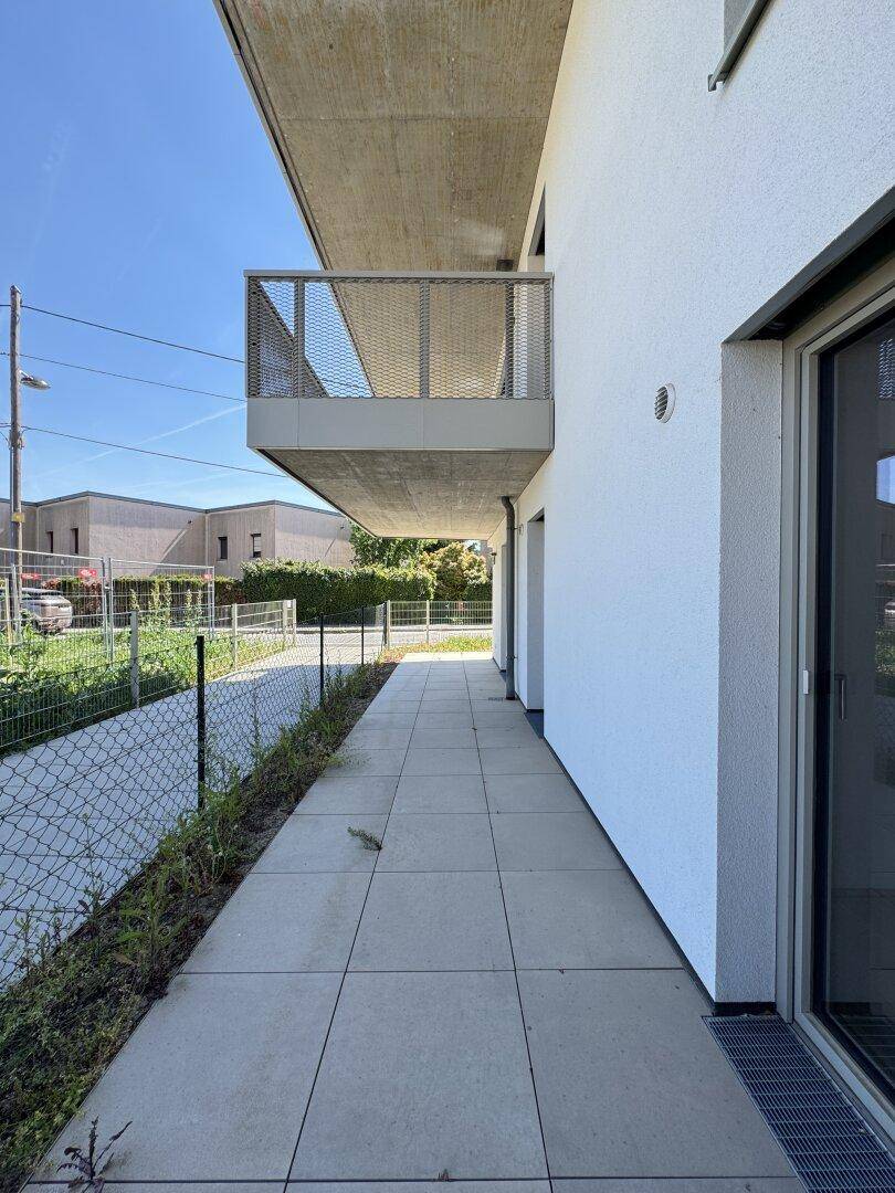 Seitenansicht des Gebäudes mit Balkon und gepflastertem Weg entlang der Fassade.