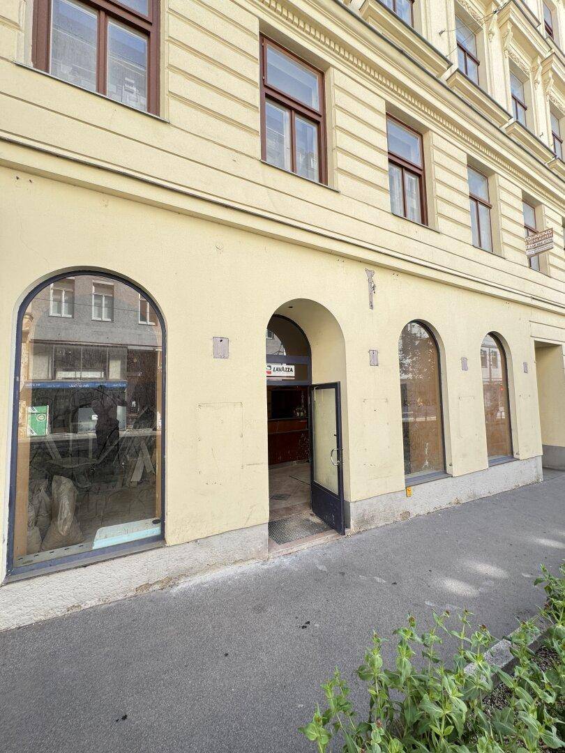 Fassade eines Altbaus mit großen Rundbogenfenstern und einem Eingang auf Straßenniveau.