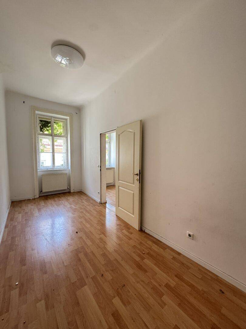 Geräumiges Zimmer mit Holzboden und Blick ins Grüne, ideal für Wohn- oder Schlafbereich in einem Altbau.