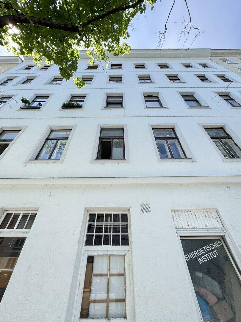 Weiße Fassade eines Altbaus mit vielen Fenstern und einem Schild, das auf ein Institut hinweist.