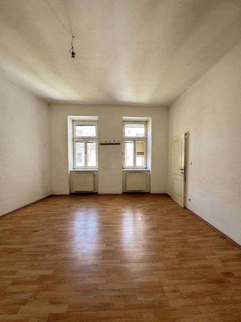 Helles, unmöbliertes Zimmer mit Holzboden und zwei Fenstern, die viel Tageslicht hereinlassen.