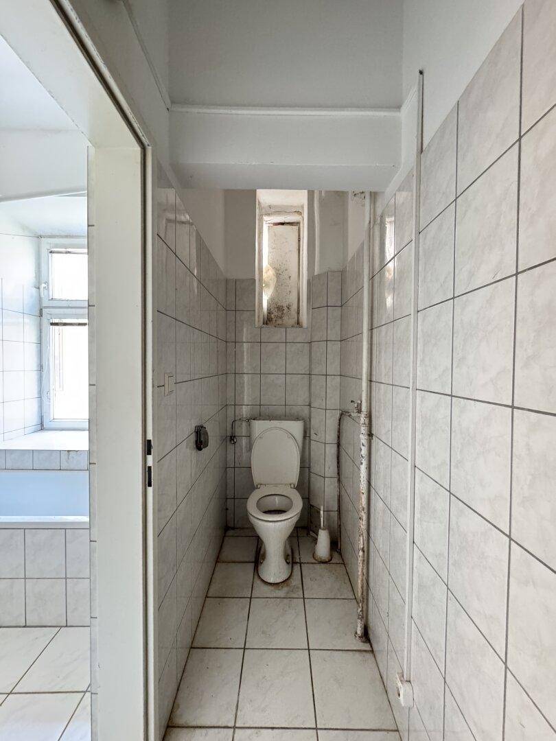 Separater WC-Bereich im Badezimmer mit Fliesen und einem kleinen Fenster, das Tageslicht spendet.