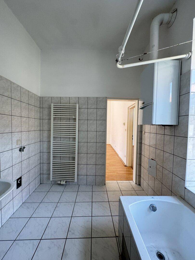 Badezimmer mit Badewanne, Handtuchheizkörper und Fliesenboden, bereit für eine Modernisierung.