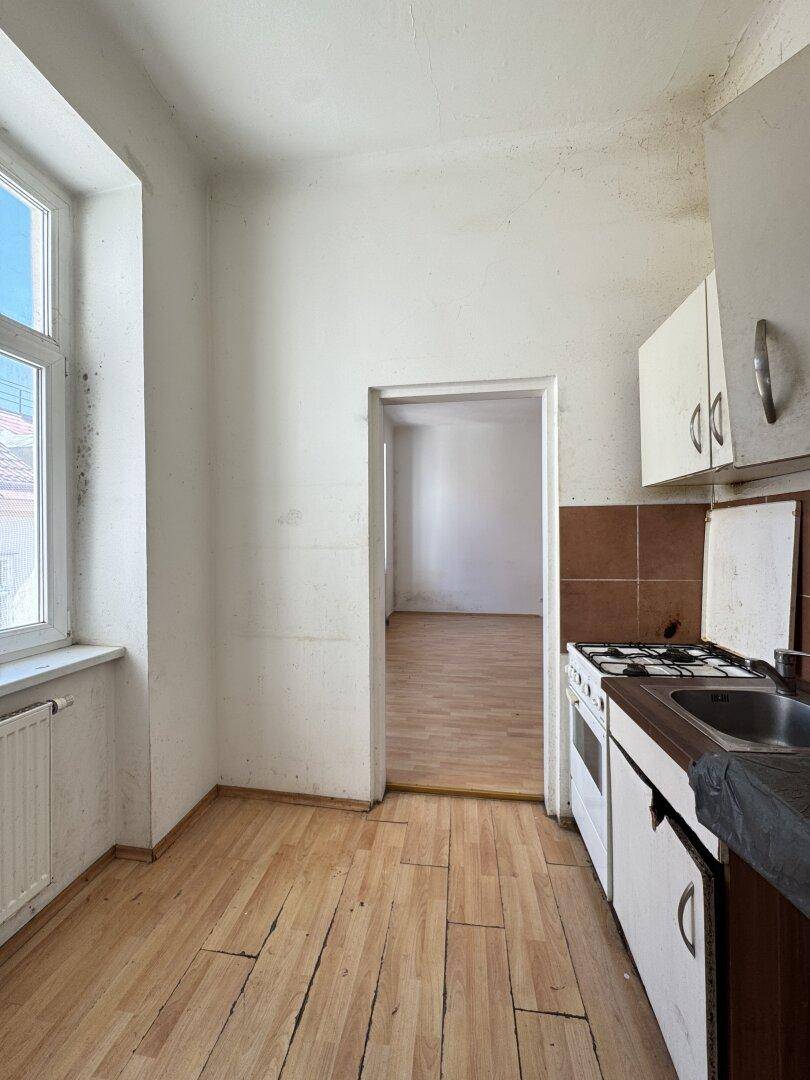 Einfache Küche mit Gasherd, Spüle und Fenster, die eine umfassende Renovierung benötigt.