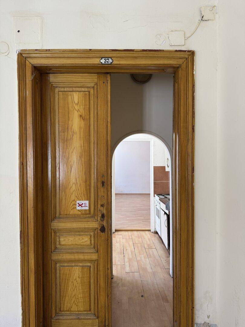 Alte Holztür mit Bogenöffnung, die in einen weiteren Raum mit Holzboden führt.
