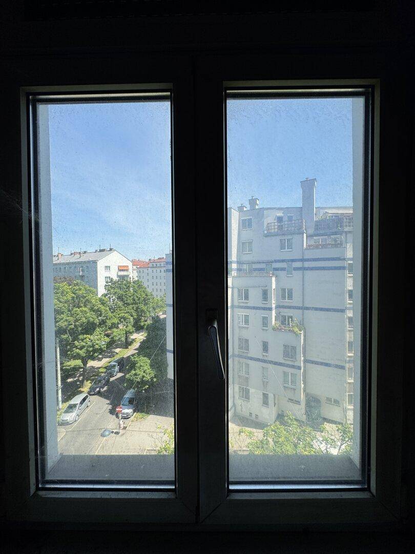 Blick aus dem Fenster auf eine belebte Straße mit Bäumen und umliegenden Gebäuden.