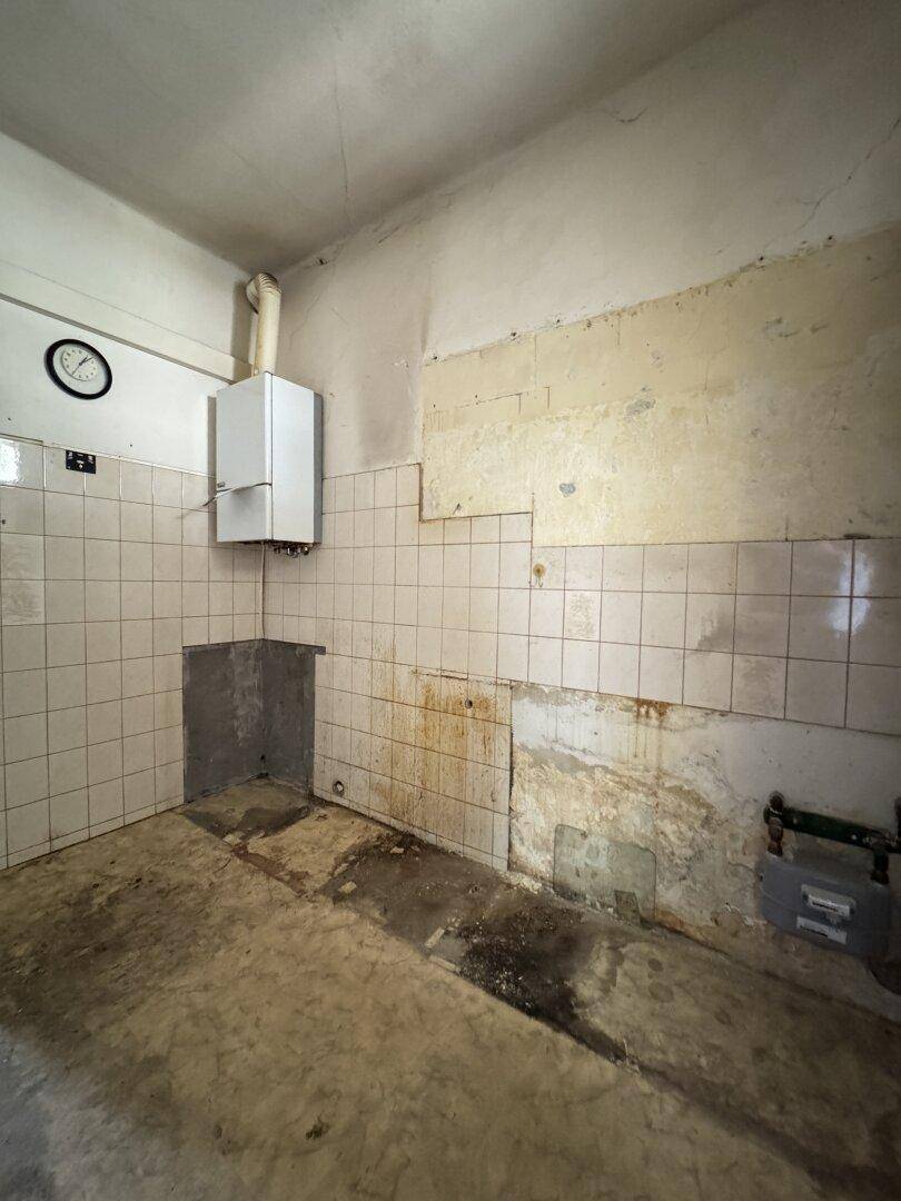 Alte Küche mit Fliesenwänden und Warmwasserbereiter, bereit für eine Modernisierung.