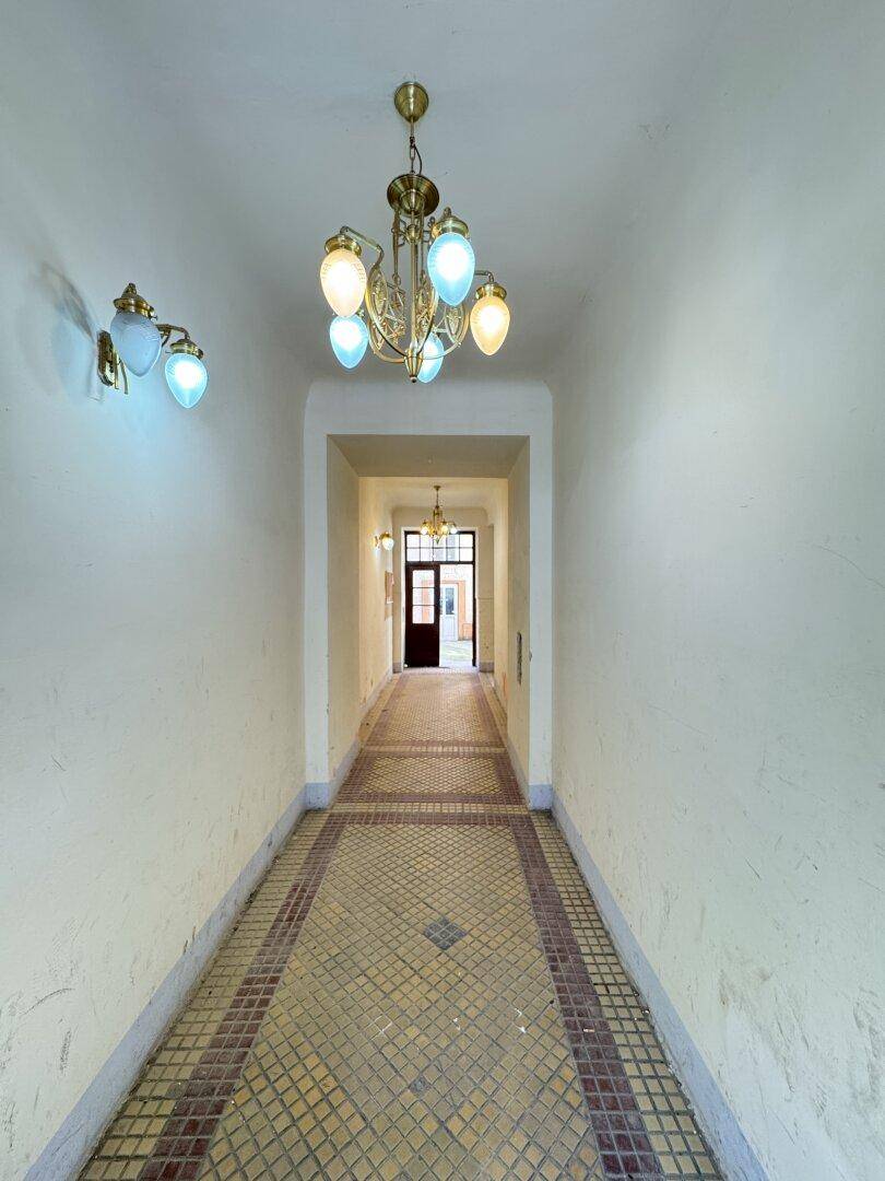 Langer Flur mit gemusterten Fliesen und dekorativen Deckenleuchten in einem Altbau.