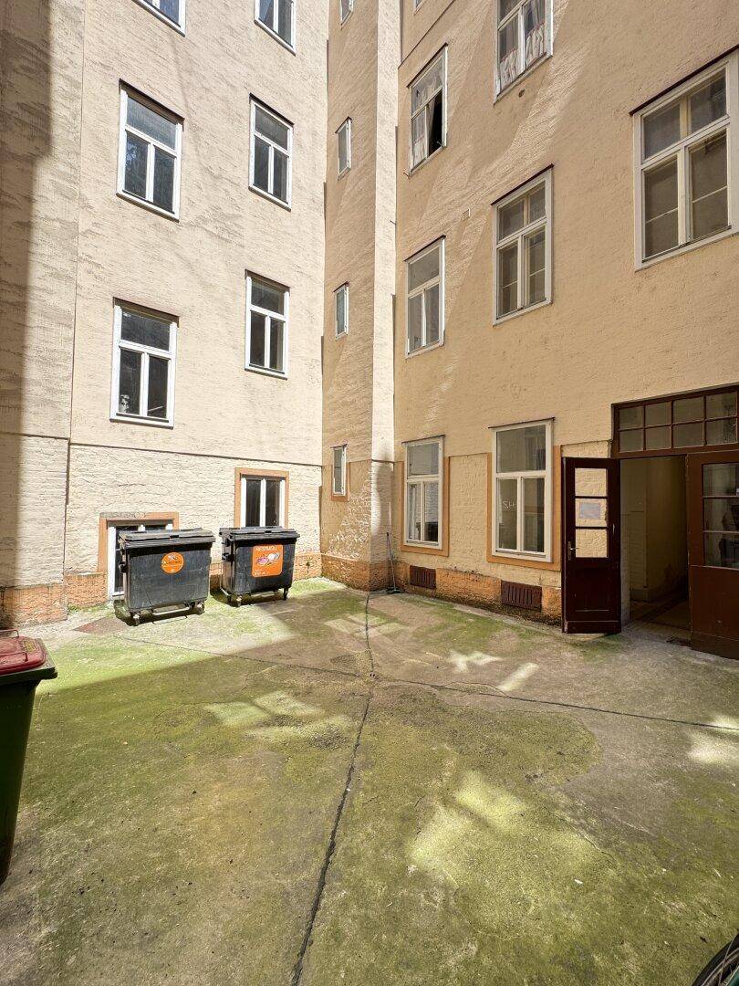 Innenhof eines Mehrfamilienhauses mit Mülltonnen und umliegenden Gebäudefassaden.