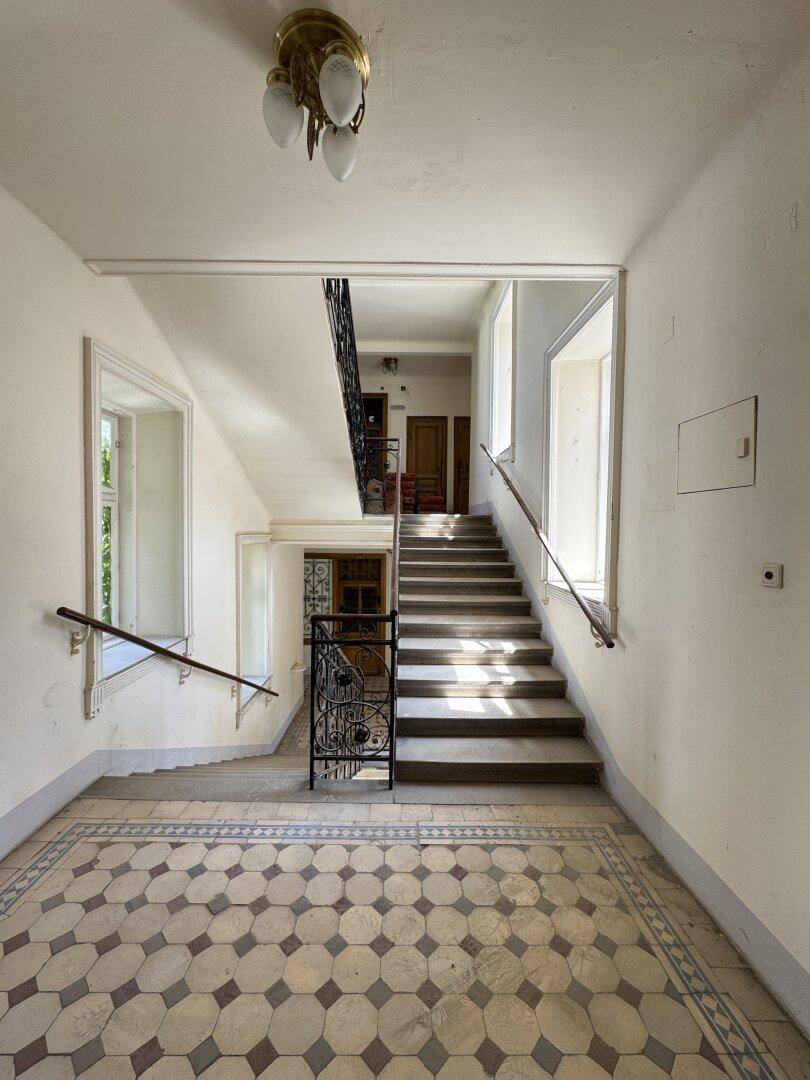 Historisches Treppenhaus mit gemustertem Fliesenboden, schmiedeeisernem Geländer und klassischem Kronleuchter.