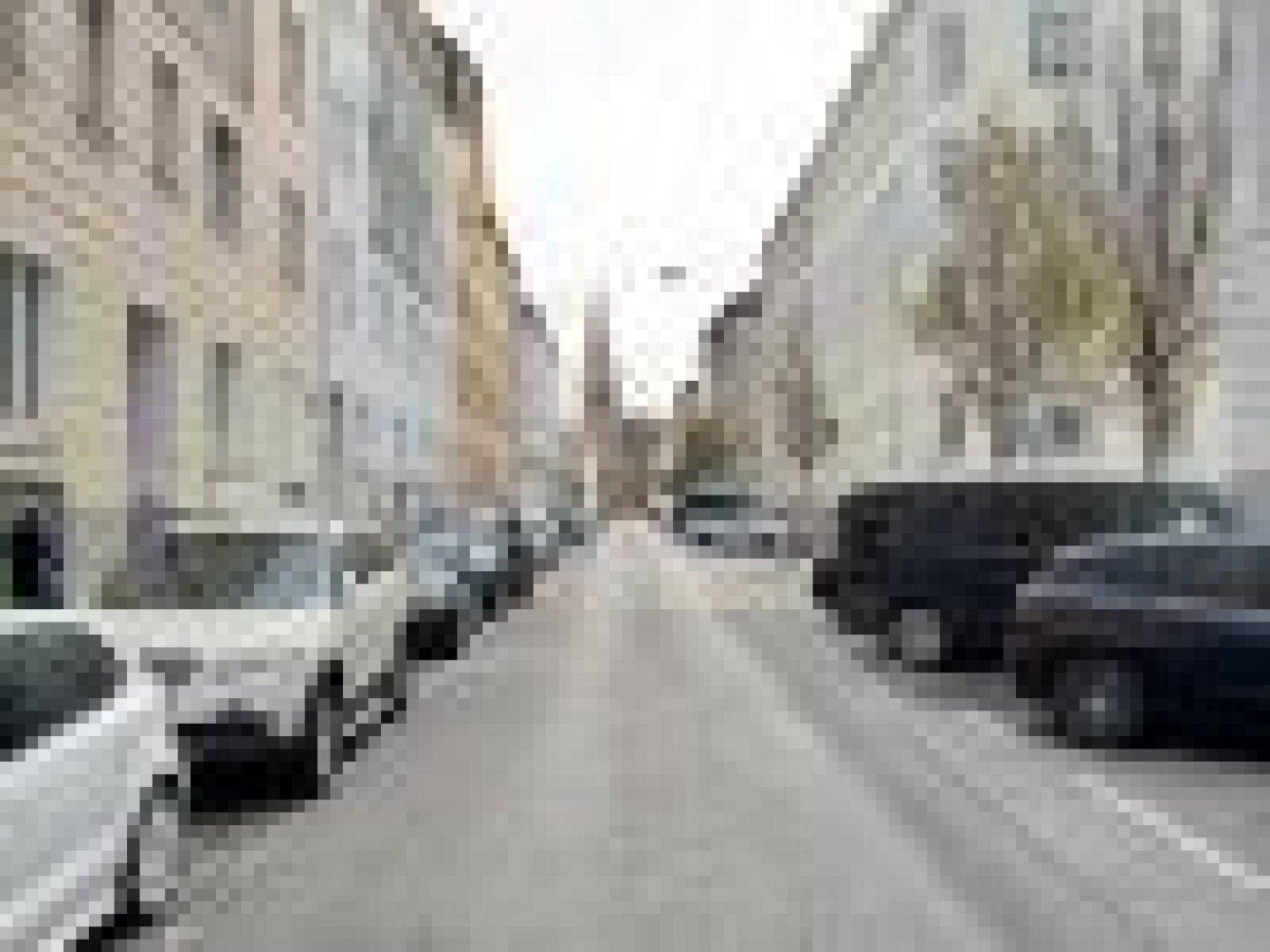Blick auf eine ruhige Stadtstraße mit parkenden Autos und historischen Gebäuden auf beiden Seiten.