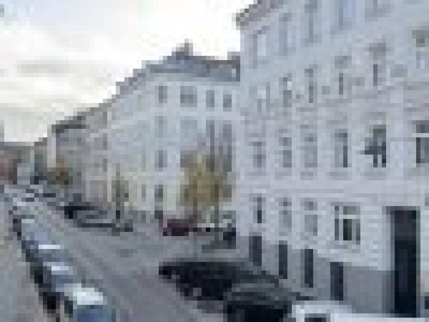 Blick auf eine belebte Stadtstraße mit eleganten weißen Gebäuden und parkenden Fahrzeugen.