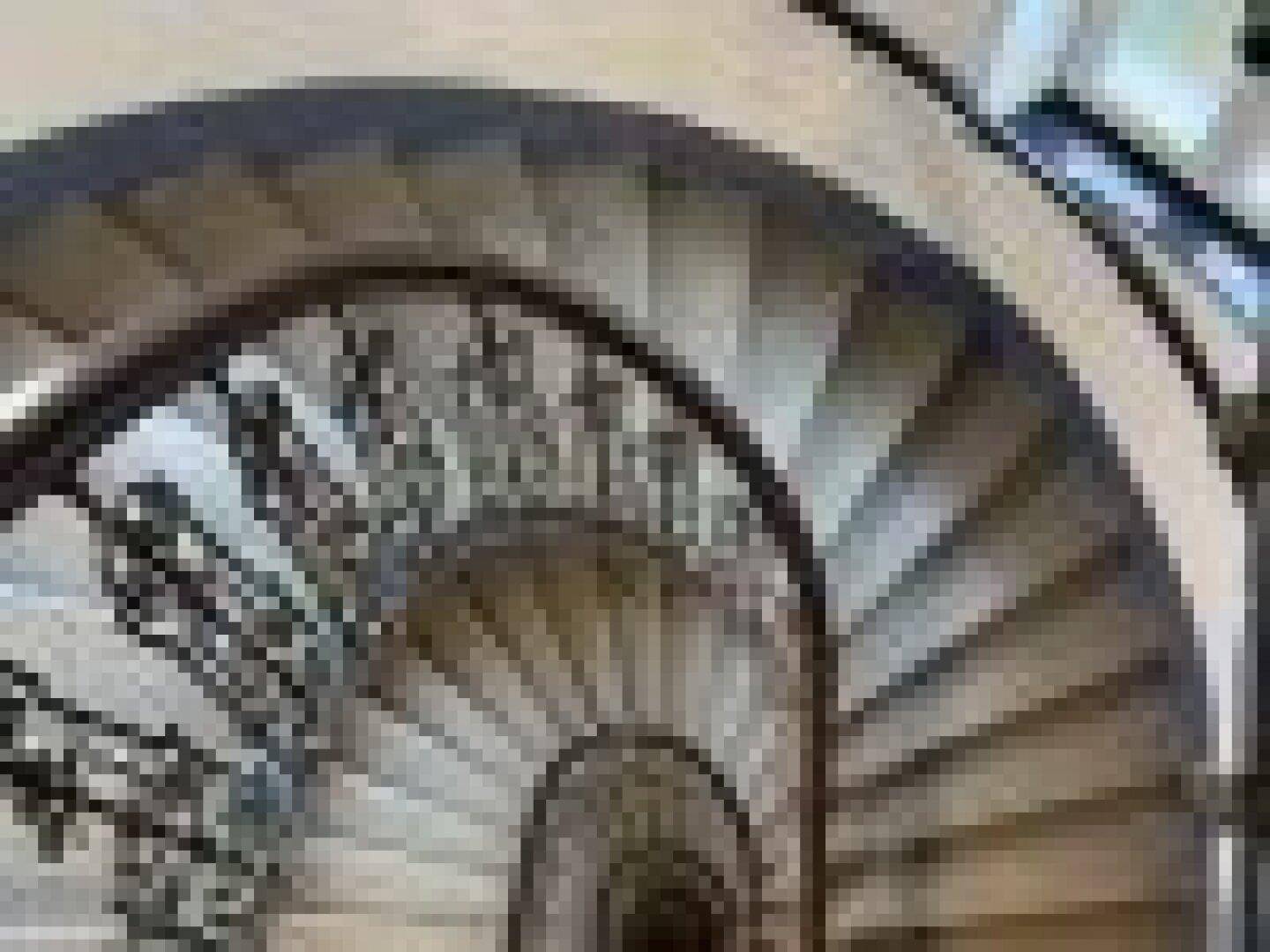 Beeindruckendes Wendeltreppenhaus mit Steinstufen und einem kunstvollen schmiedeeisernen Geländer.