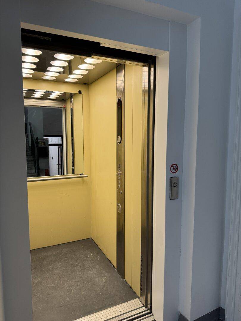 Moderner Aufzug mit Spiegelflächen und heller Beleuchtung im Gebäude.