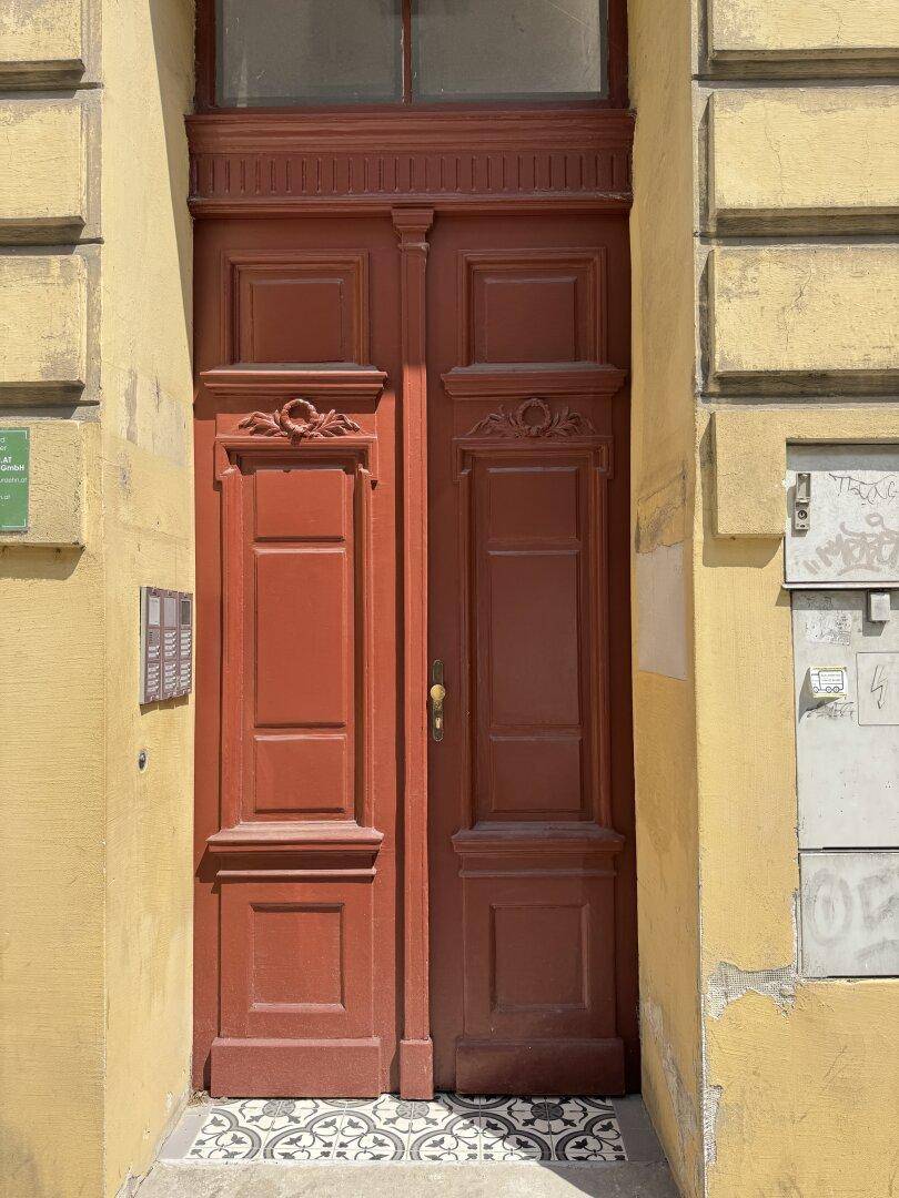Historische Eingangstür mit aufwendigen Schnitzereien in einer gelben Fassade.