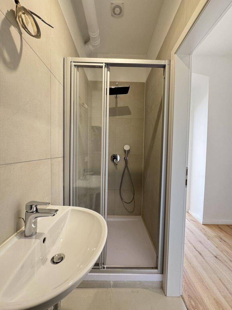 Modernes Badezimmer mit Duschkabine, Waschbecken und hellen Fliesen an Wänden und Boden.