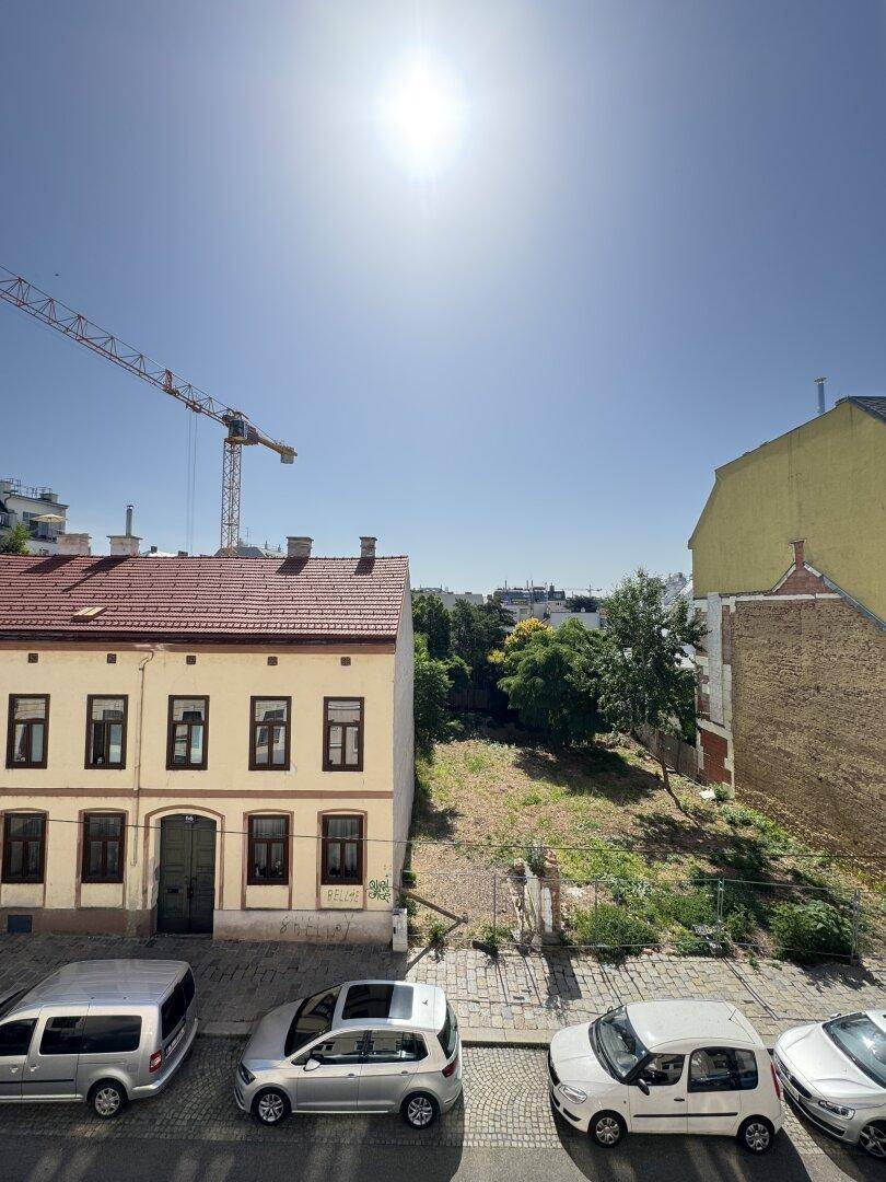 Blick von oben auf eine Straße mit parkenden Autos, ein altes Gebäude und eine freie Fläche.