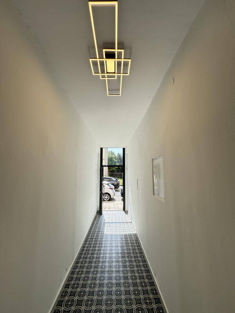 Heller Flur mit gemustertem Fliesenboden und moderner Deckenleuchte, die den Eingangsbereich beleuchtet.