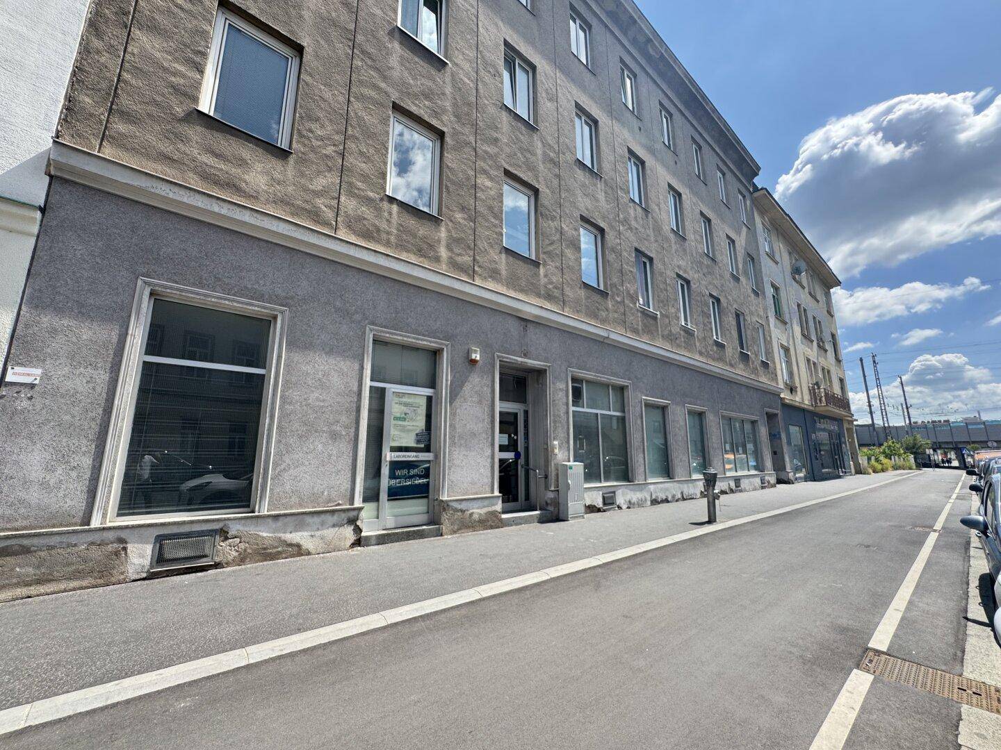 Nahaufnahme der Fassade eines älteren Gebäudes mit Geschäften im Erdgeschoss und parkenden Autos.