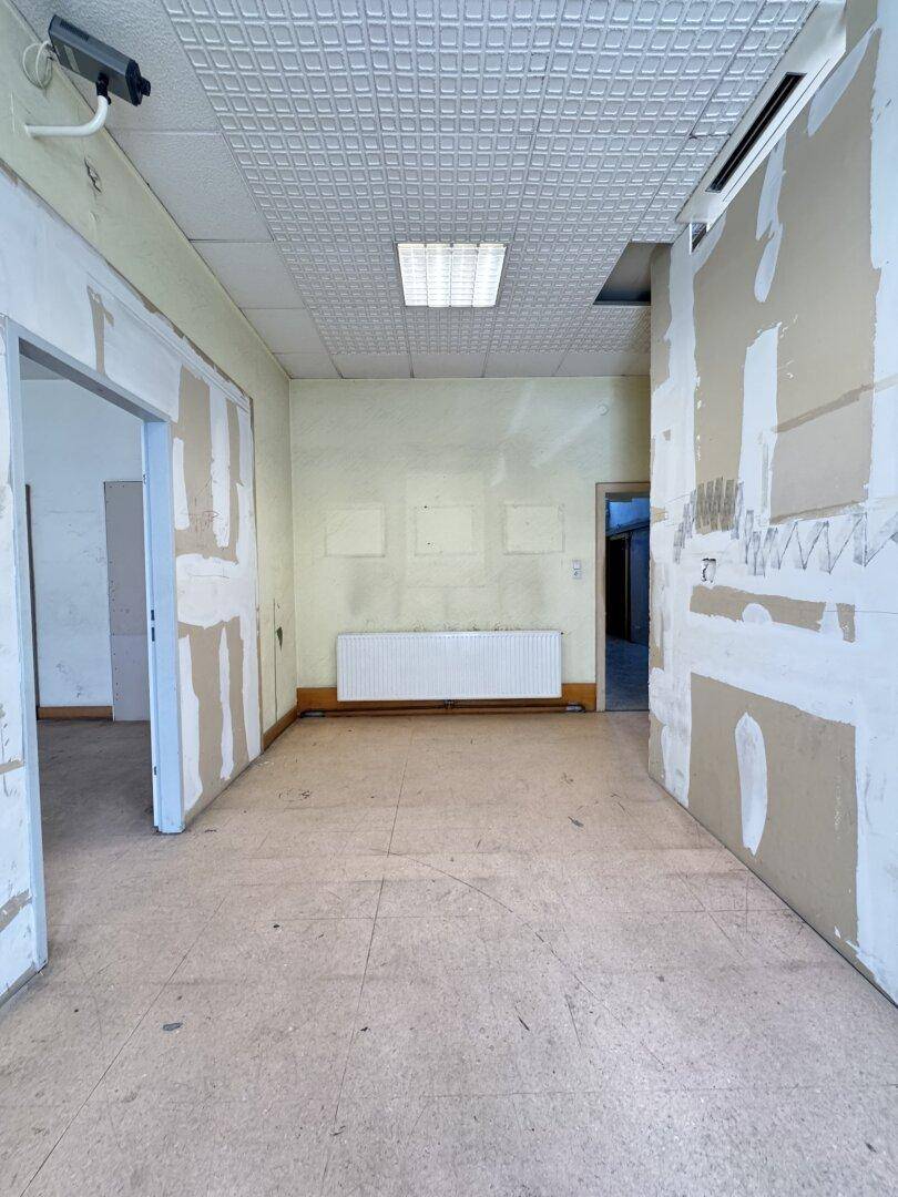 Renovierungsbedürftiger Raum mit abgehängter Decke, Heizkörper und sichtbaren Trockenbauwänden.