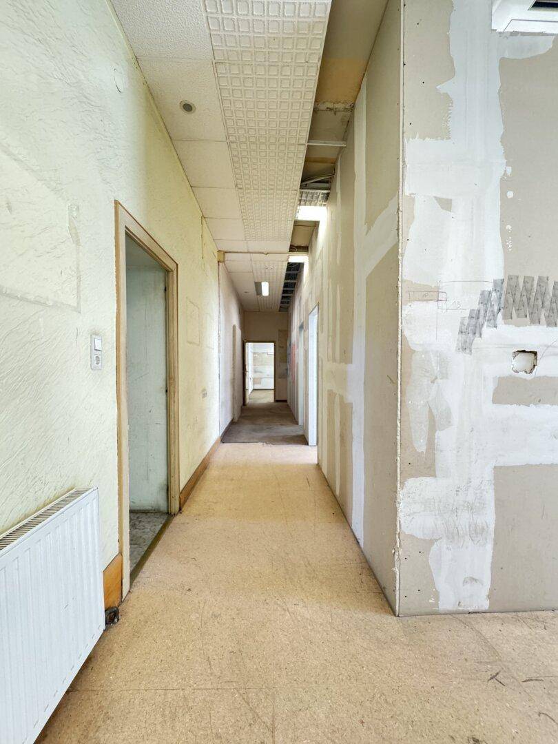 Langer Flur mit abgehängter Decke und Wänden, die für Renovierungsarbeiten vorbereitet sind.