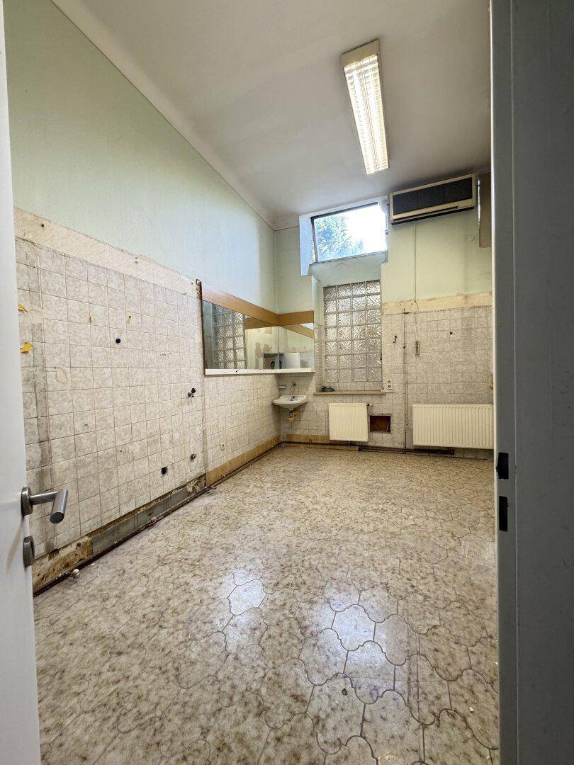 Badezimmer mit alten Fliesen, Waschbecken und Fenster, das eine umfassende Renovierung benötigt.