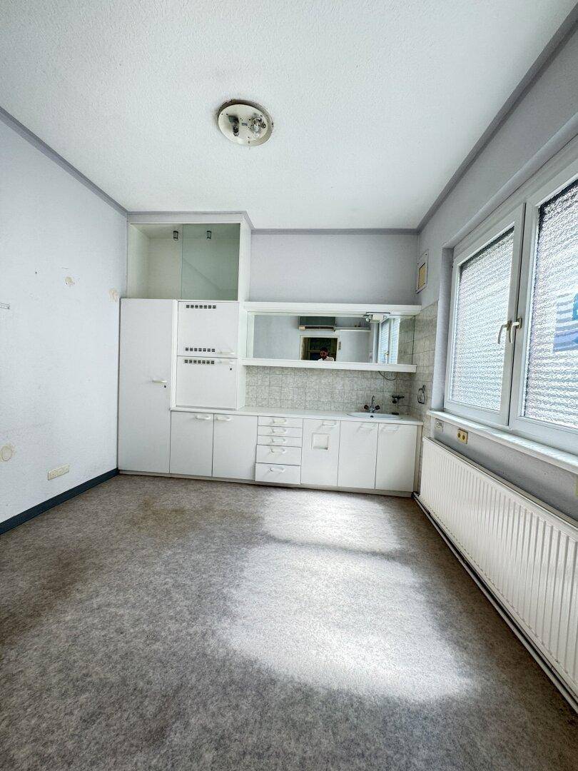 Kleine Küche mit weißen Schränken, Spüle und Fenster, die eine Modernisierung erfordert.