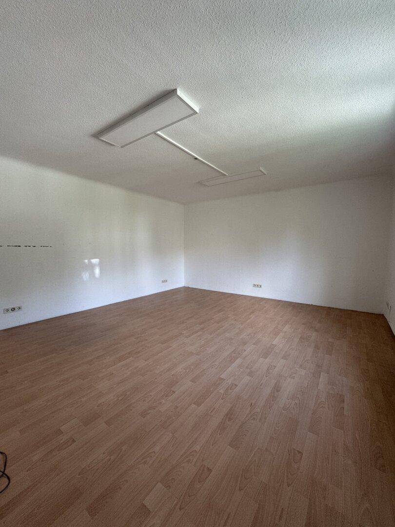 Heller, leerer Raum mit Laminatboden und modernen Deckenleuchten, bereit für die Nutzung.