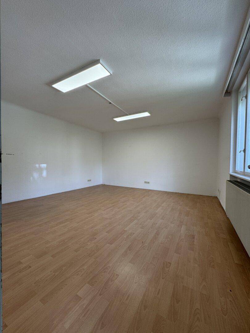 Geräumiger, heller Raum mit Laminatboden und großen Fenstern, ideal für Bürozwecke.