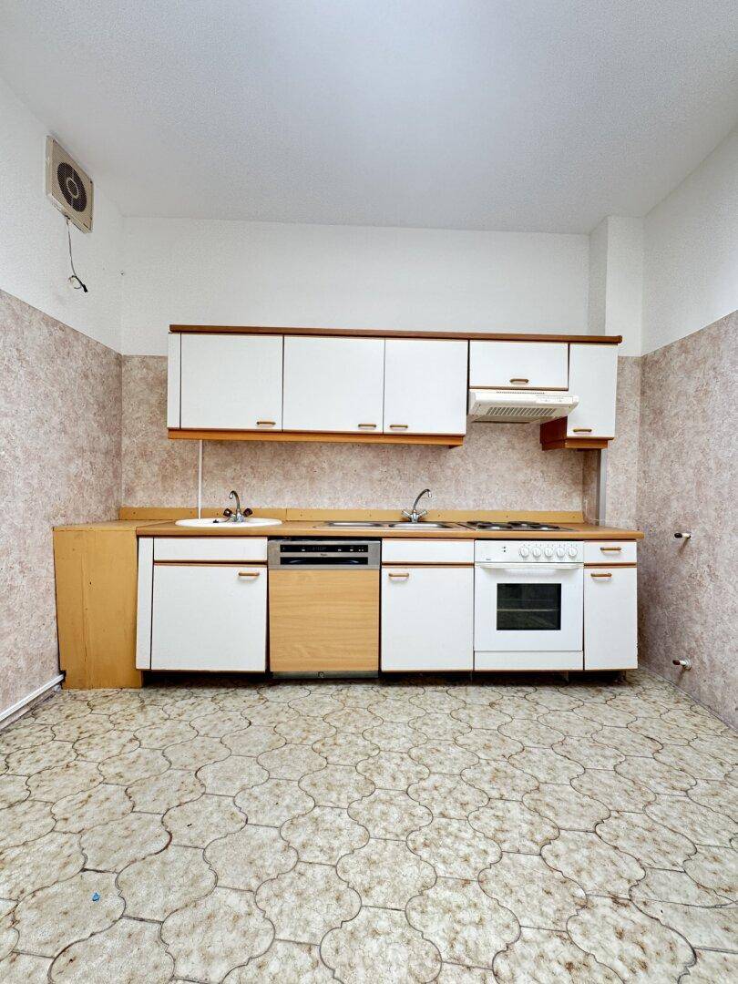 Ältere Einbauküche mit weißen Schränken, Spüle und Herd, die eine Modernisierung benötigt.