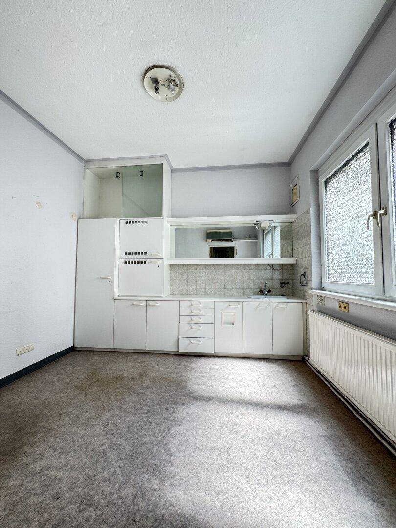 Kleine Küche mit weißen Schränken, Spüle und Fenster, die eine Modernisierung erfordert.
