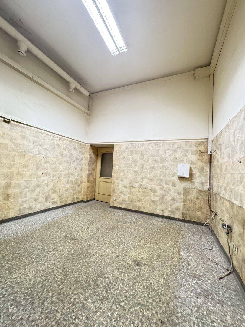 Leerer Raum mit Mosaikfliesenboden und teilweise gefliesten Wänden, der Renovierung benötigt.