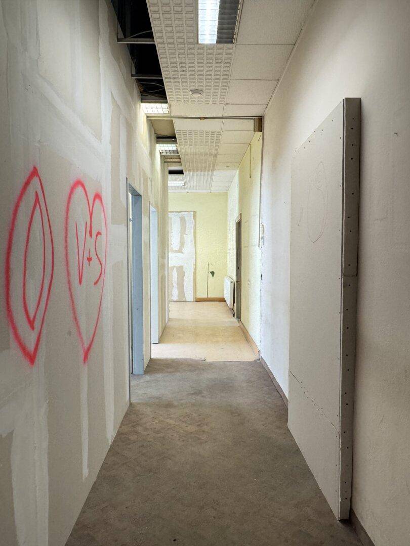 Langer Flur mit Trockenbauwänden und Deckenplatten, der auf weitere Renovierungsarbeiten wartet.