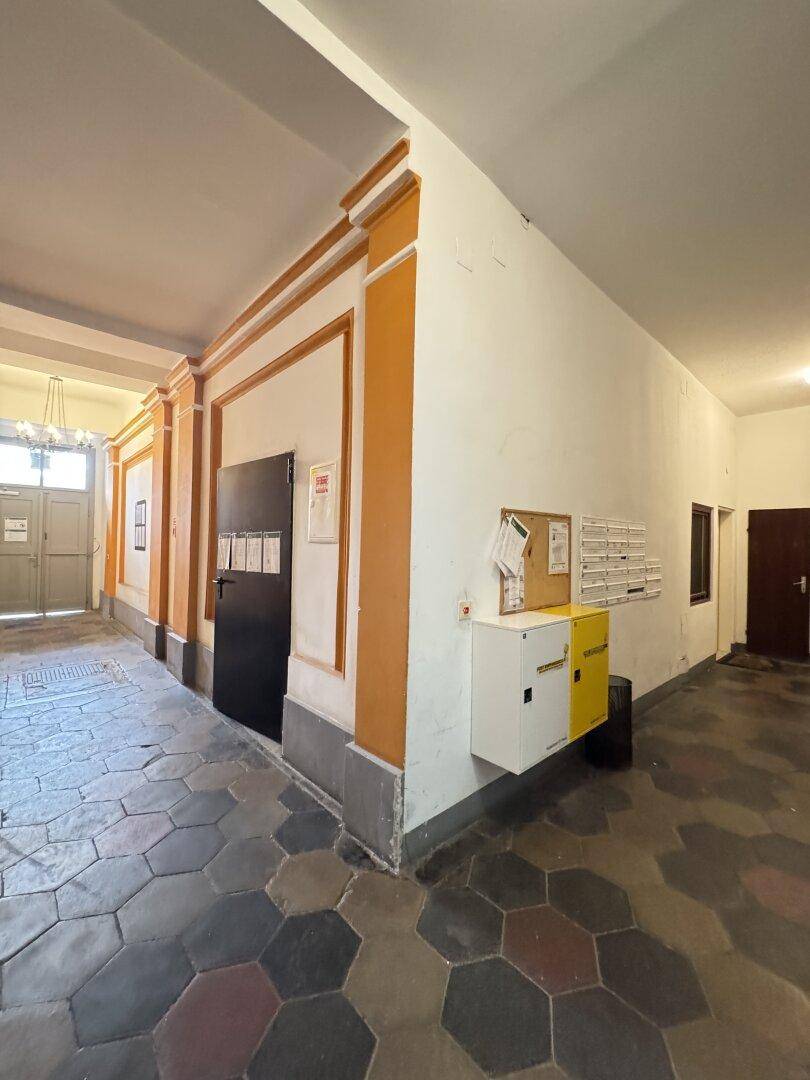 Geräumiger Eingangsbereich mit historischen Fliesen, Postfächern und Anschlagtafel.